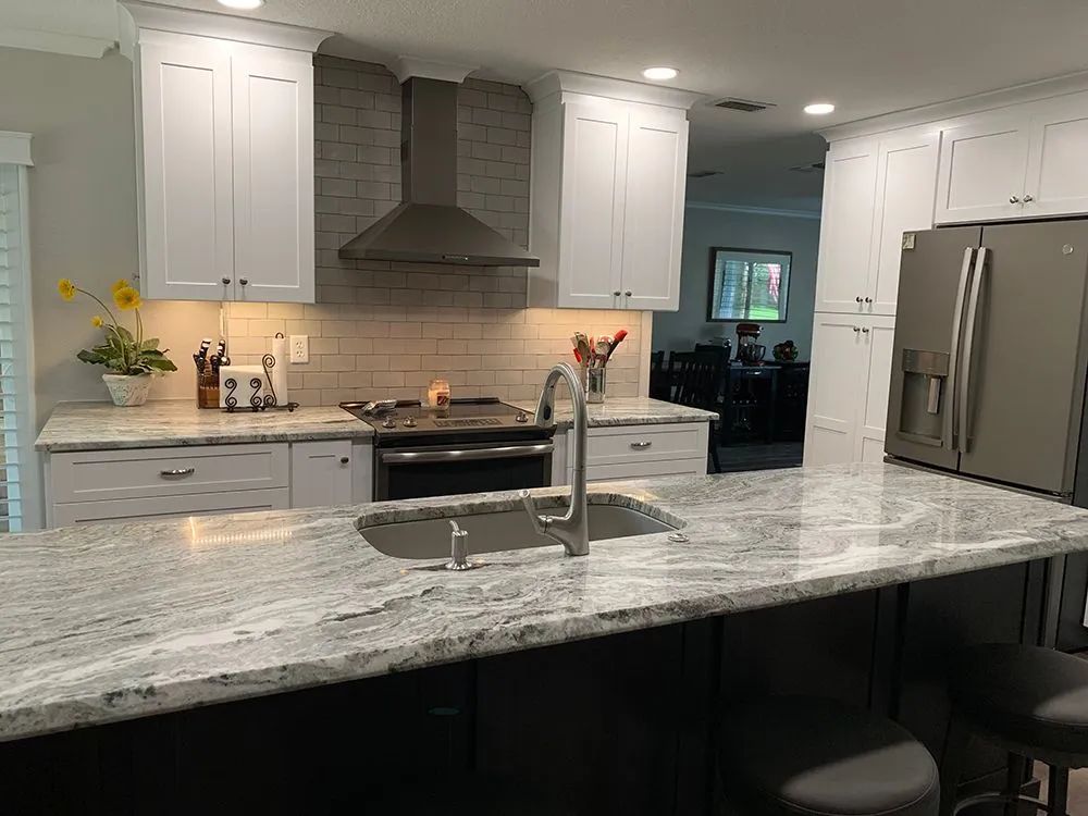Bright modern kitchen with white cabinets, gray island, stainless steel appliances, and marble countertops