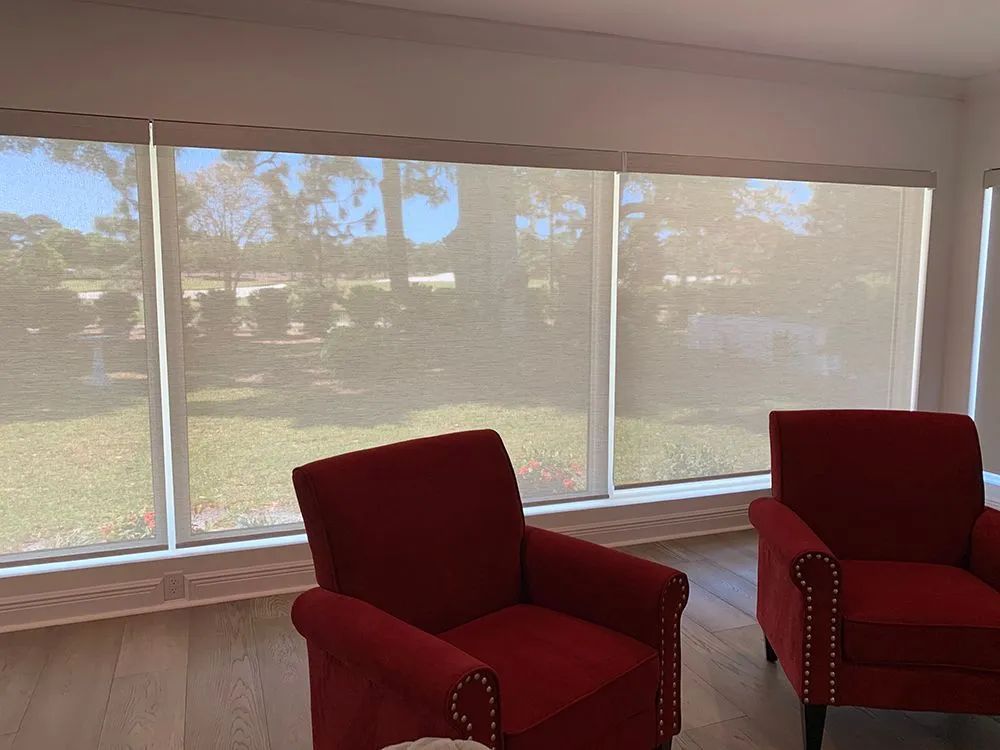 Sunlit room with large windows, red upholstered chairs, and a grassy view outside