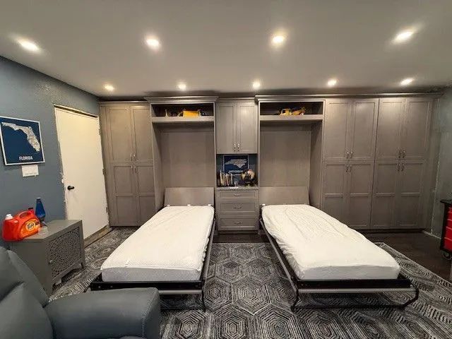 Gray bedroom with two twin beds, built-in cabinets, recessed lights, and patterned dark carpet.