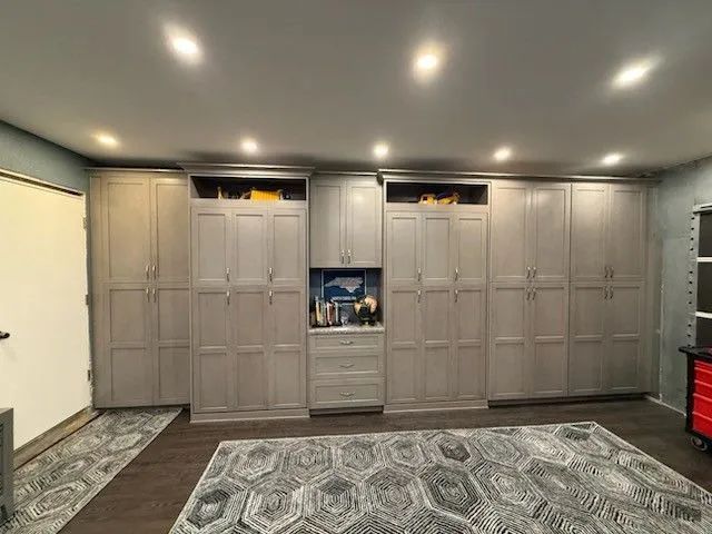Built-in gray cabinets and drawers in a room with recessed ceiling lights and patterned floor rugs