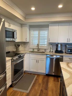 Modern kitchen with stainless steel appliances, white cabinets, gray countertops, and a window over the sink