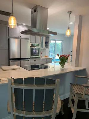 Bright modern kitchen with white island, stainless steel appliances, pendant lights, and turquoise chairs