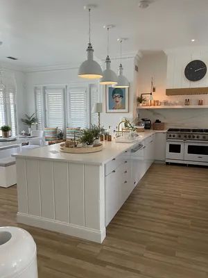 Bright white kitchen with island, pendant lights, wood floors, and stainless-steel stove.