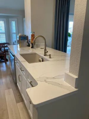 Modern white kitchen island with double sink, chrome faucet, and dark curtains by a window