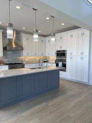 Modern kitchen with dark island, white cabinets, stainless appliances, and light wood flooring