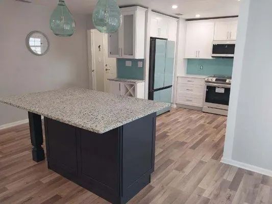 Modern kitchen with granite island, light wood floors, teal pendant lights, and white cabinets