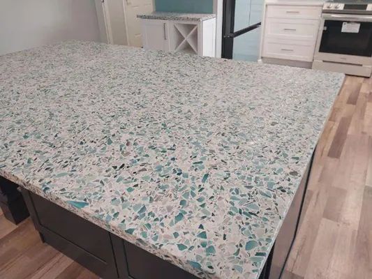 Large speckled stone kitchen island countertop with wood flooring and white cabinets nearby
