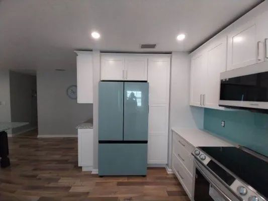 Modern kitchen with white cabinets, blue island, stainless steel appliances, and wood floors