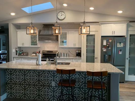 Modern kitchen with island, bar stools, pendant lights, and a clock above the counters