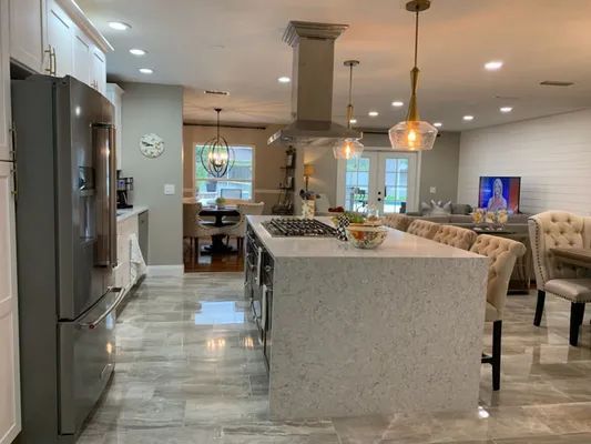 Bright modern kitchen with island, stainless fridge, pendant lights, and adjoining dining and living area