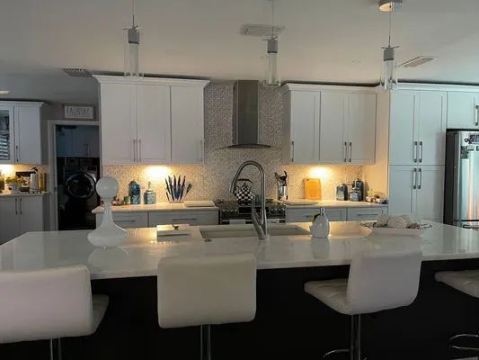 Modern white kitchen with island, pendant lights, bar stools, and stainless steel appliances