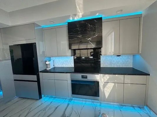 Modern white kitchen with black countertops, stainless appliances, and blue under-cabinet lighting