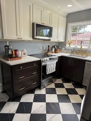 Modern kitchen with white cabinets, black lower cabinets, checkered floor, stove, microwave, and window sink.