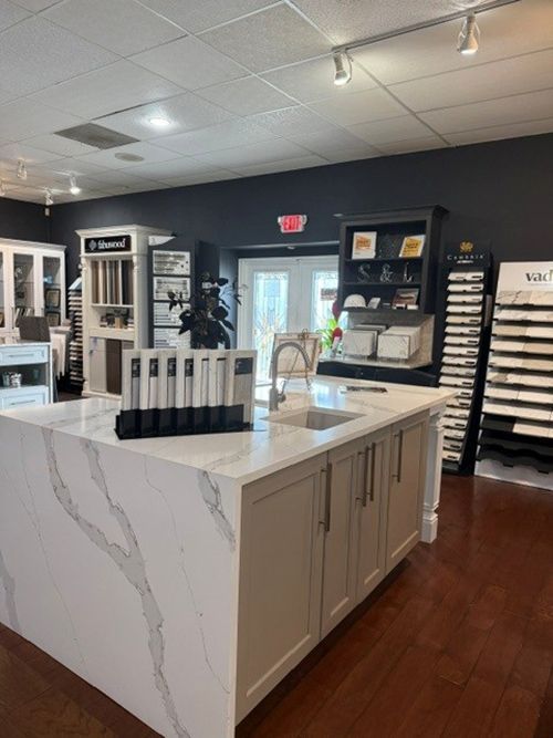 Modern showroom with a white marble island, wood floor, and wall displays of fixtures and samples.