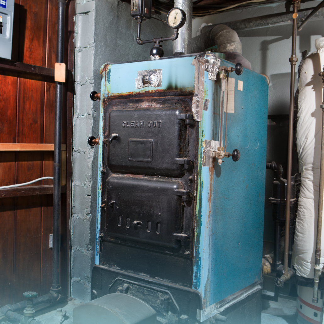 A vintage, light blue industrial furnace in a basement setting with visible piping, a pressure gauge, and two metal doors.