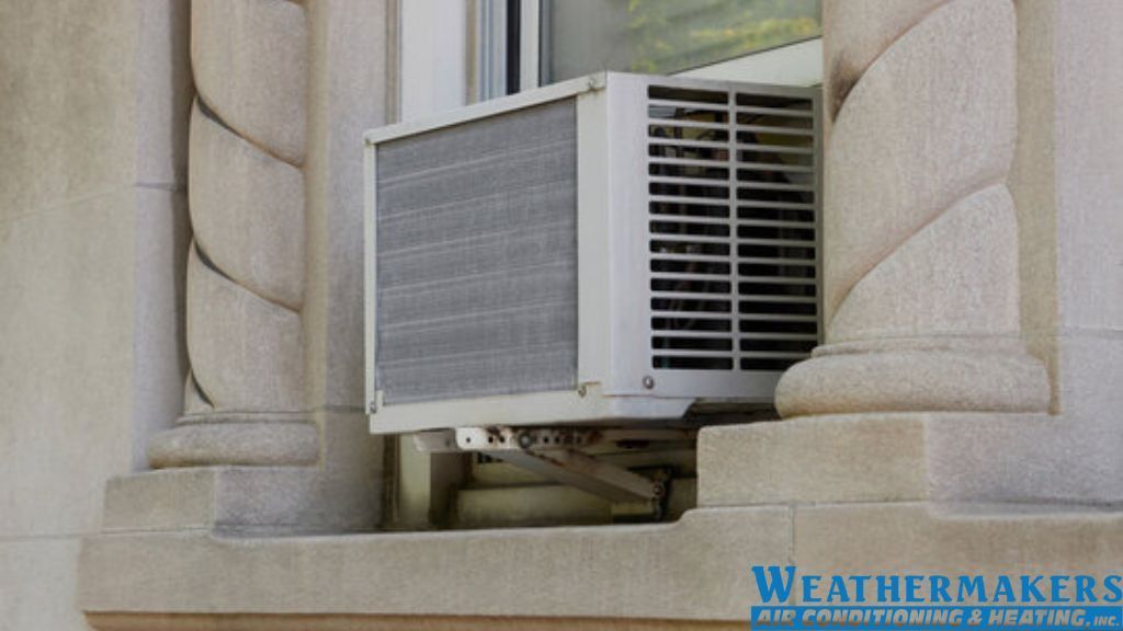 A window-mounted air conditioning unit installed in an exterior stone frame with decorative pillars.