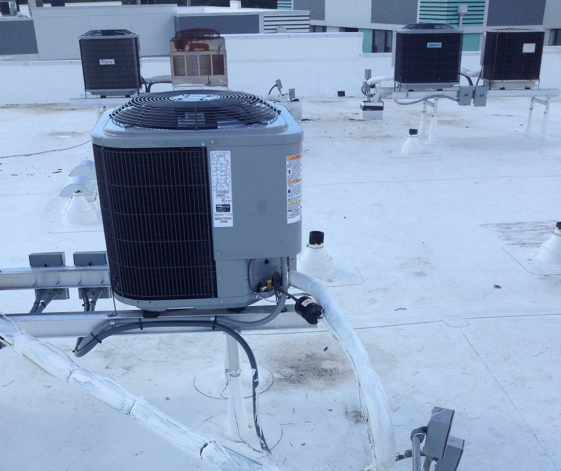 Multiple grey air conditioning units installed on a white commercial rooftop.
