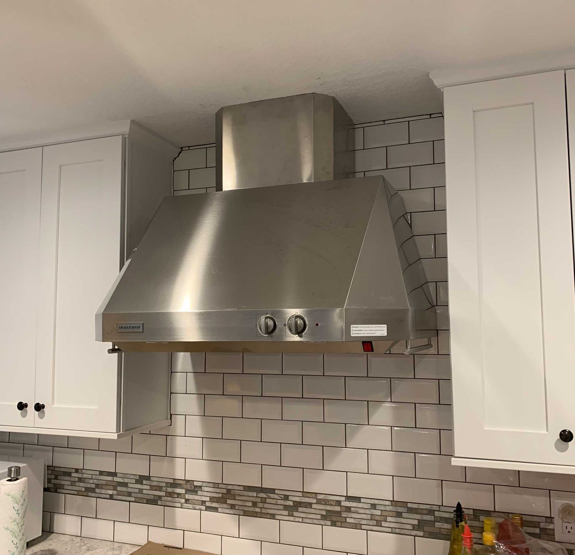 A stainless steel range hood installed between two white kitchen cabinets above a subway tile backsplash.