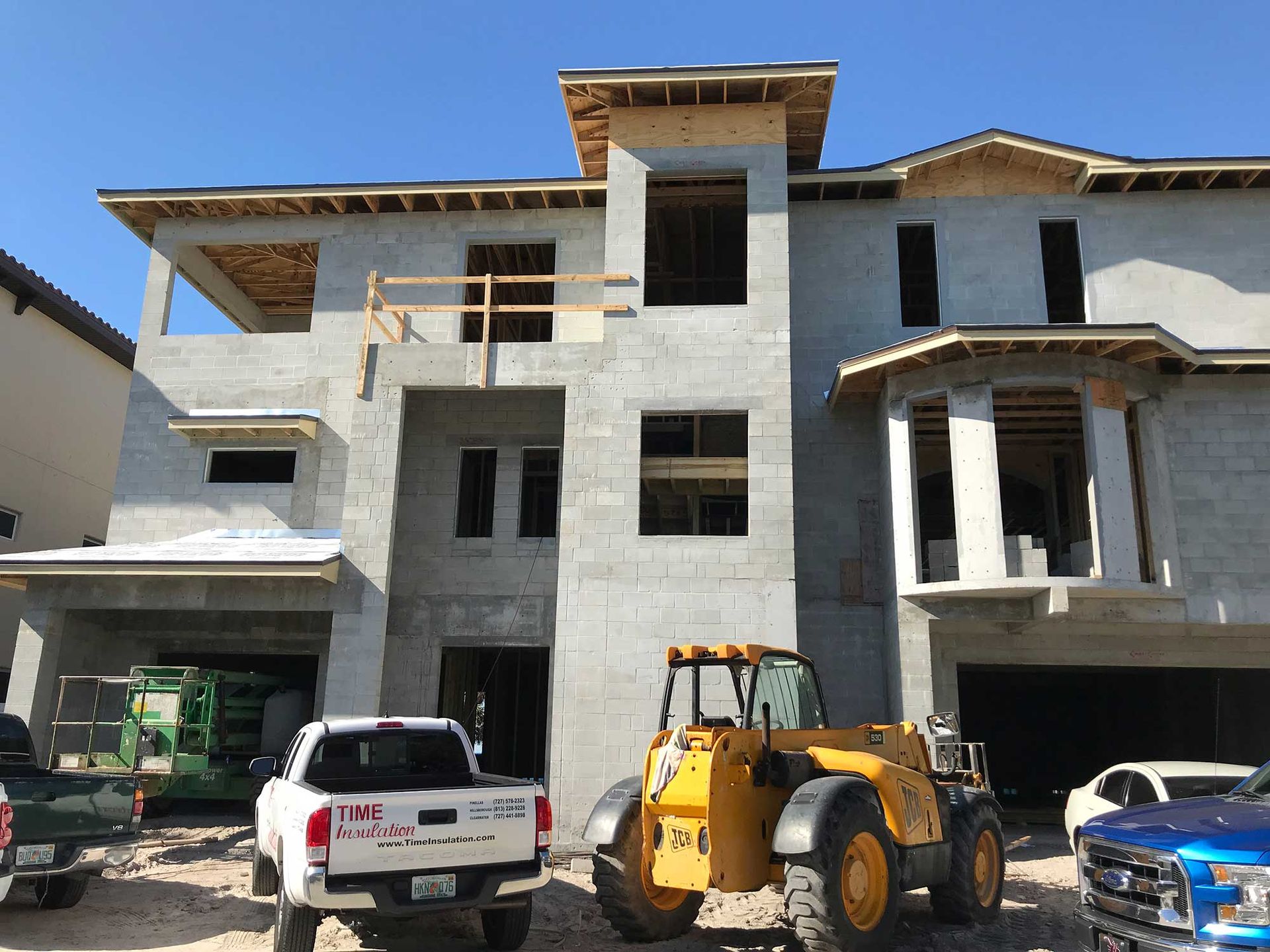 A multi-story building under construction with concrete walls, open window frames, and construction equipment parked ahead.