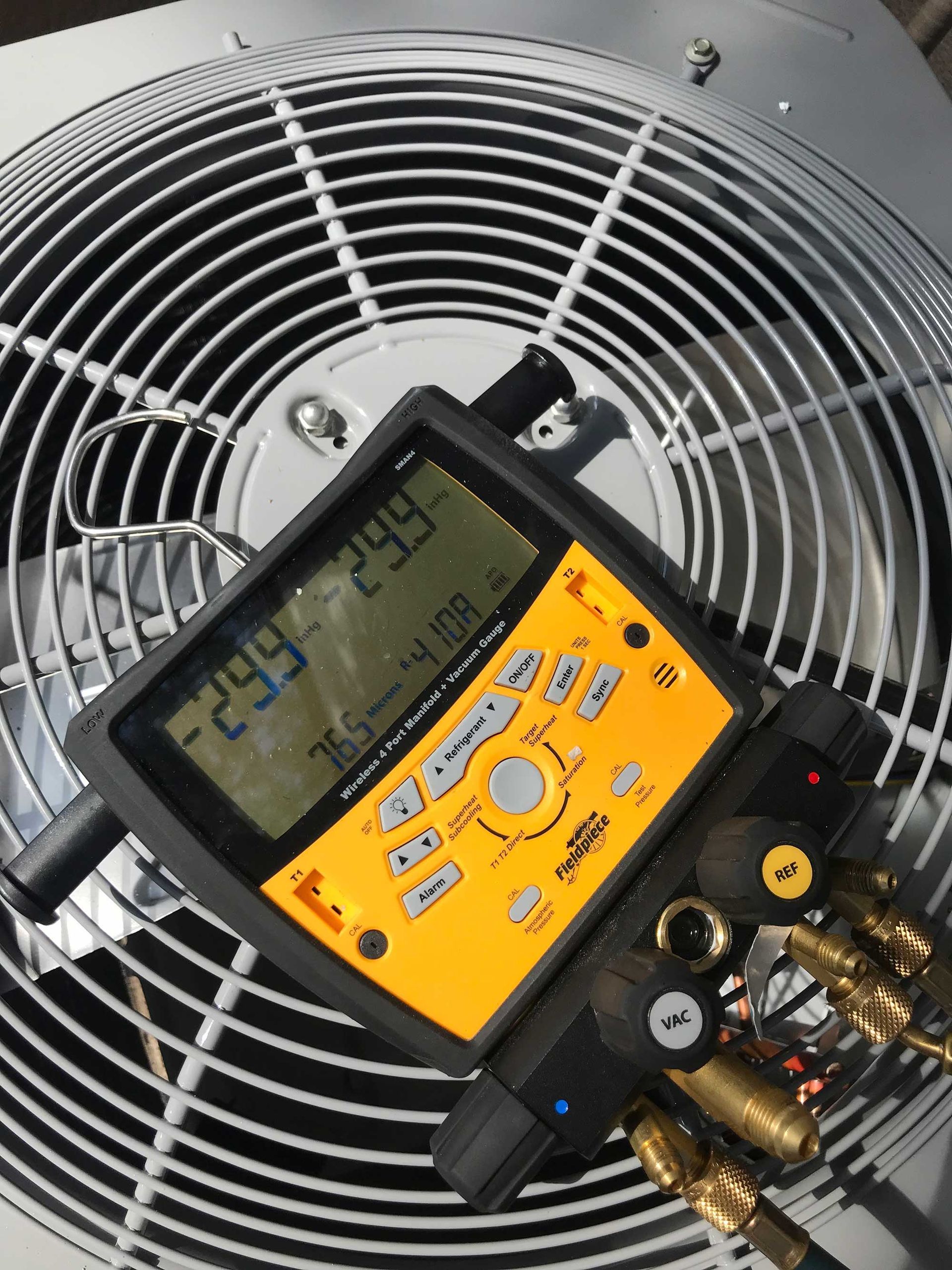 A digital HVAC pressure gauge set resting on a metal outdoor air conditioning unit fan grill.