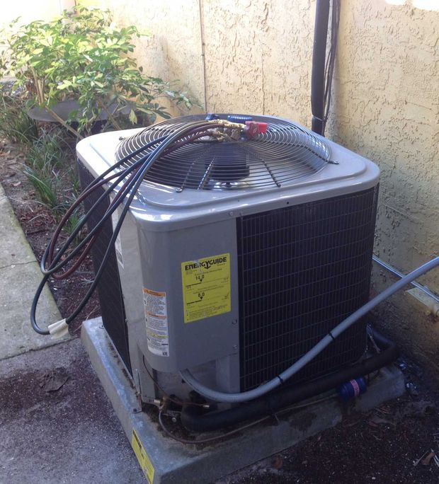 An outdoor gray residential air conditioning unit sitting on a concrete pad next to a beige exterior wall.