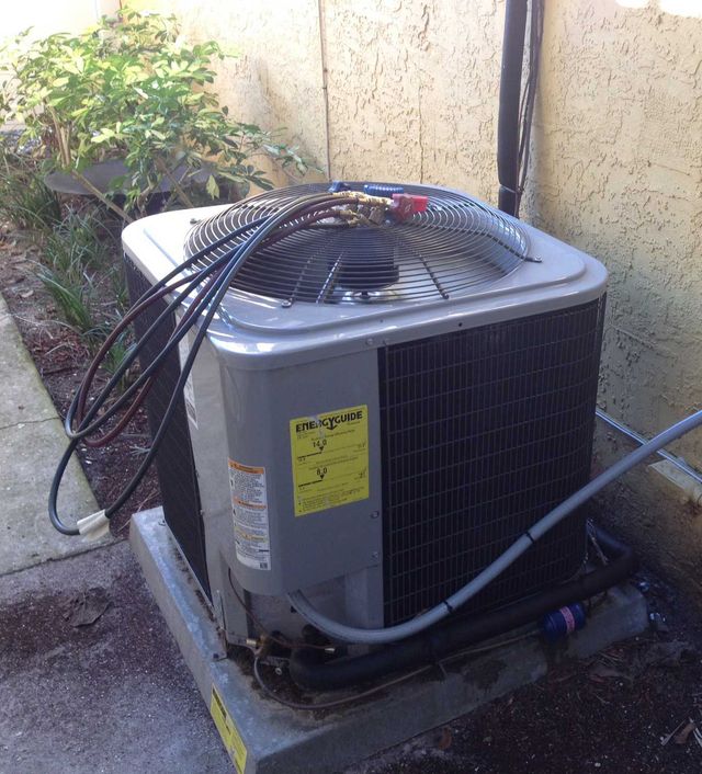 An outdoor gray residential air conditioning unit sitting on a concrete pad next to a beige exterior wall.