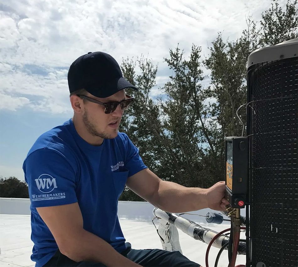 Technician in blue shirt and black cap working on rooftop HVAC unit outdoors.