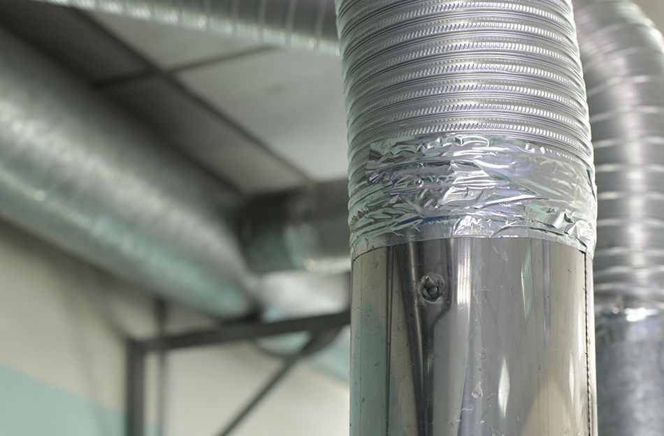 Close-up of a silver HVAC duct taped to a metal pipe in an industrial ceiling space.
