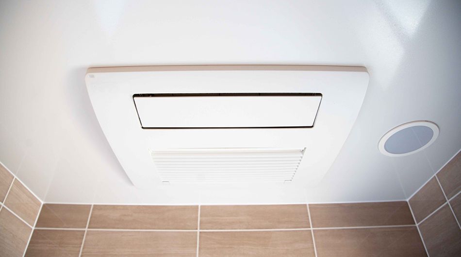 White bathroom ceiling vent above beige tile wall with a round recessed light