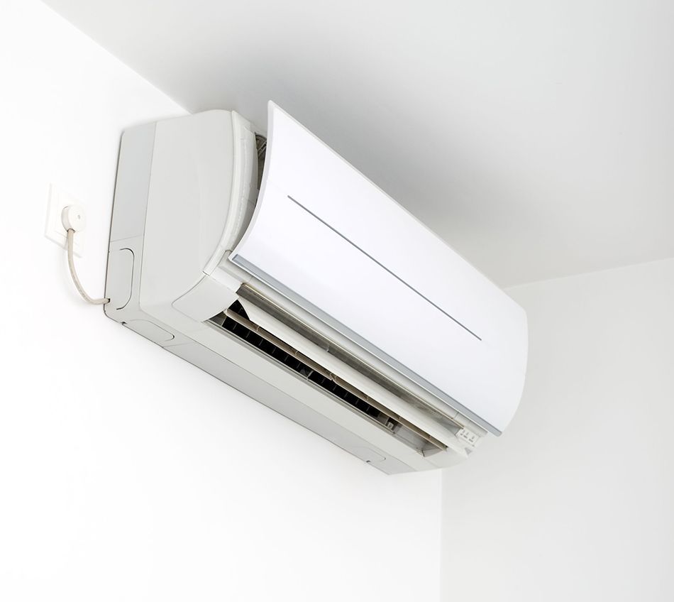 Wall-mounted white air conditioner near the ceiling in a bright room.