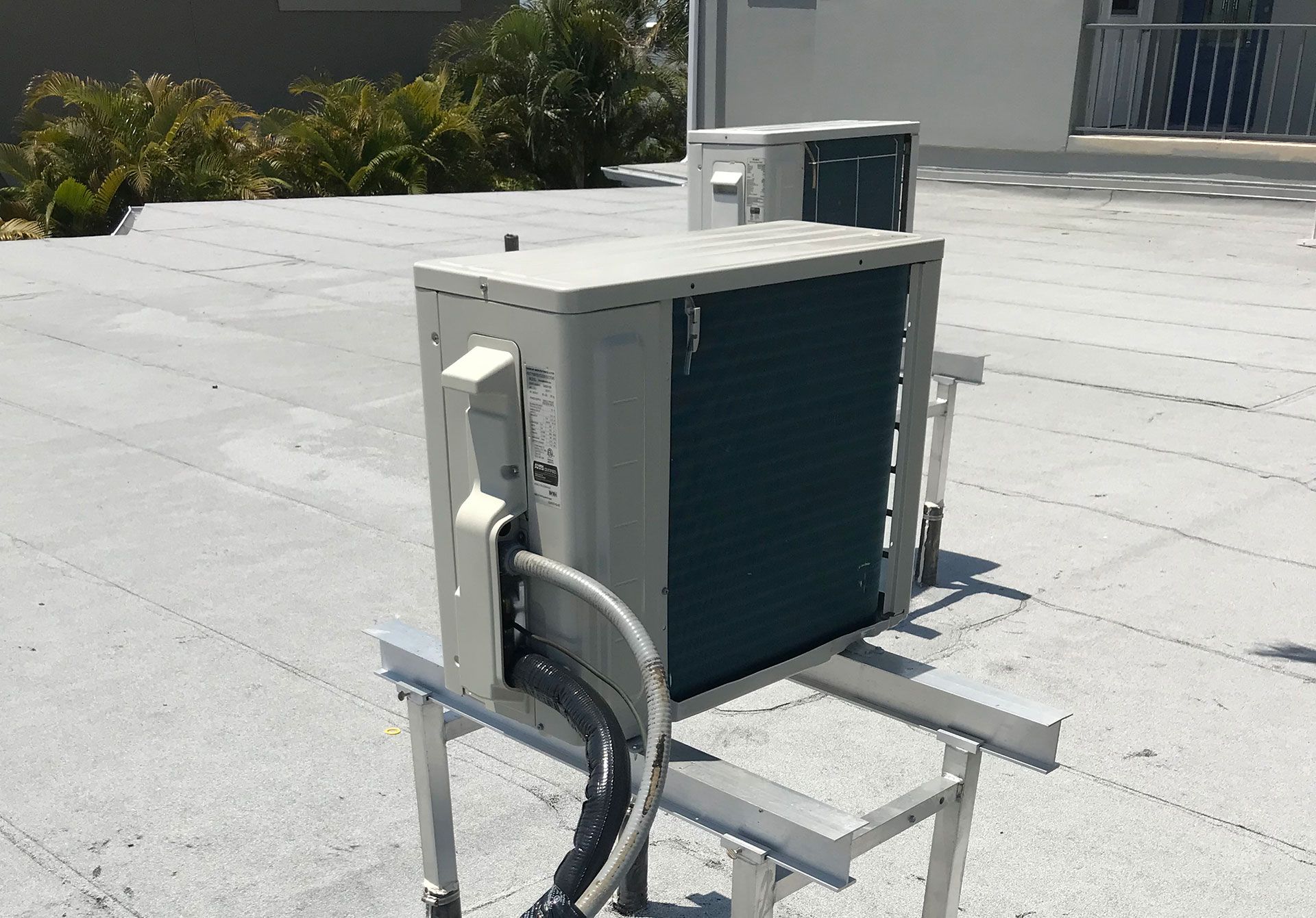 Two beige air conditioning condenser units mounted on metal stands on a flat, light-colored roof.