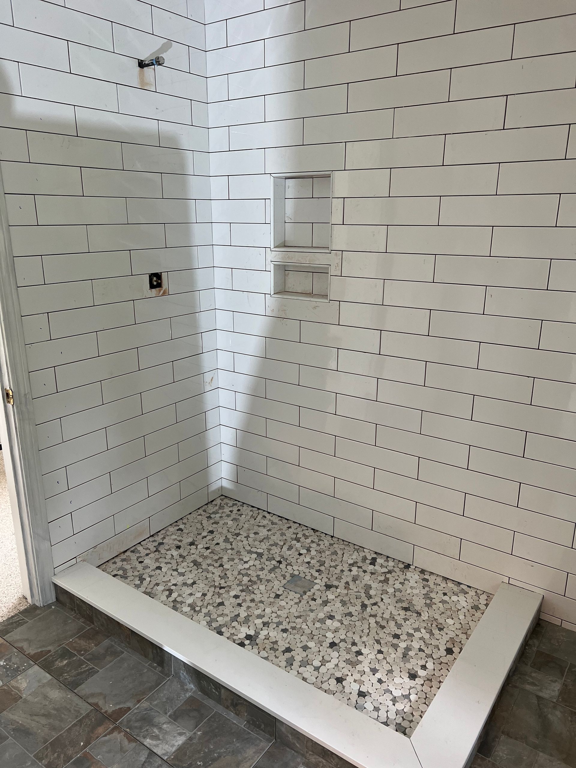 A shower stall in a bathroom with white tiles on the wall.