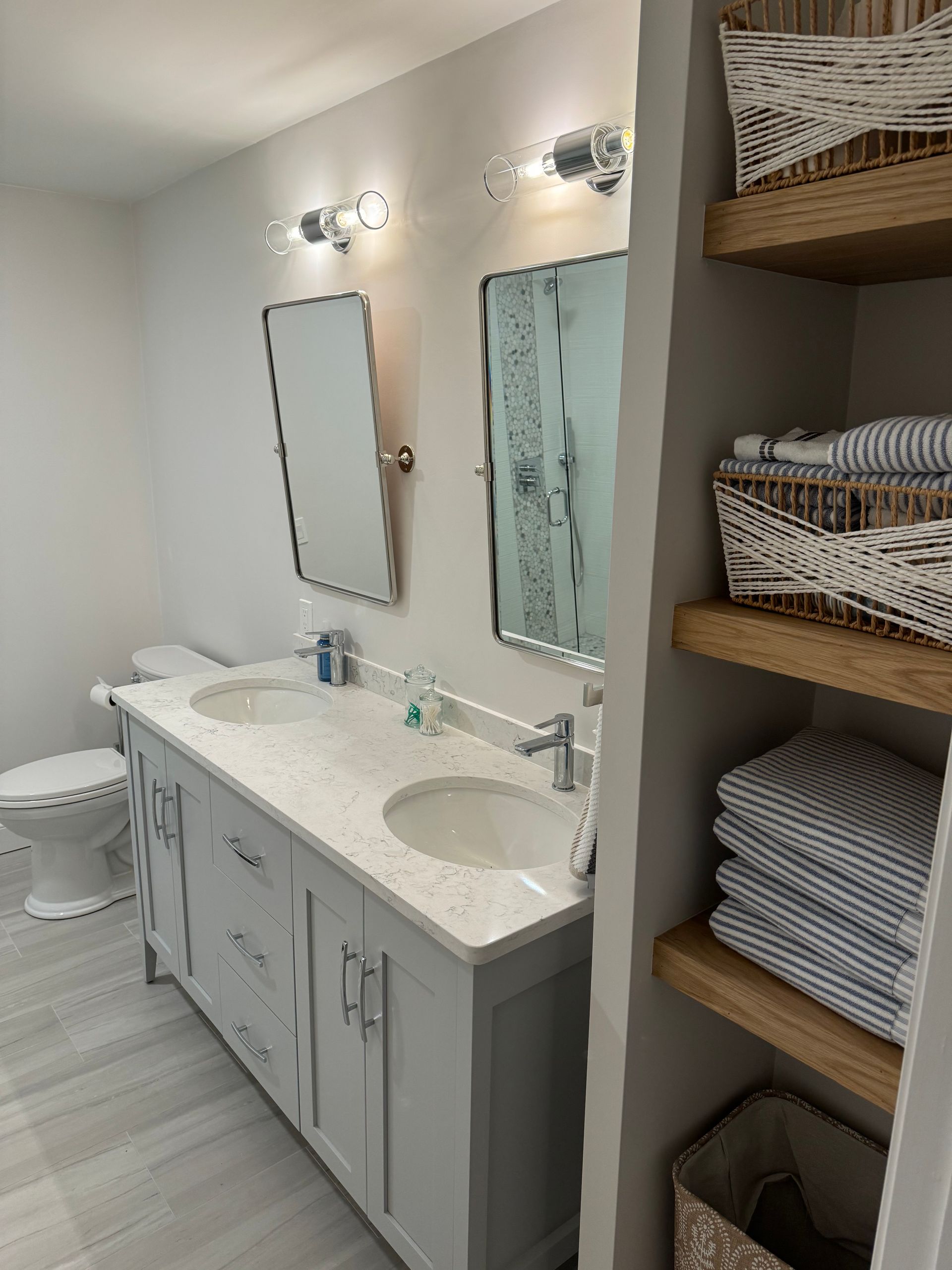 A bathroom with two sinks , two mirrors and a toilet.