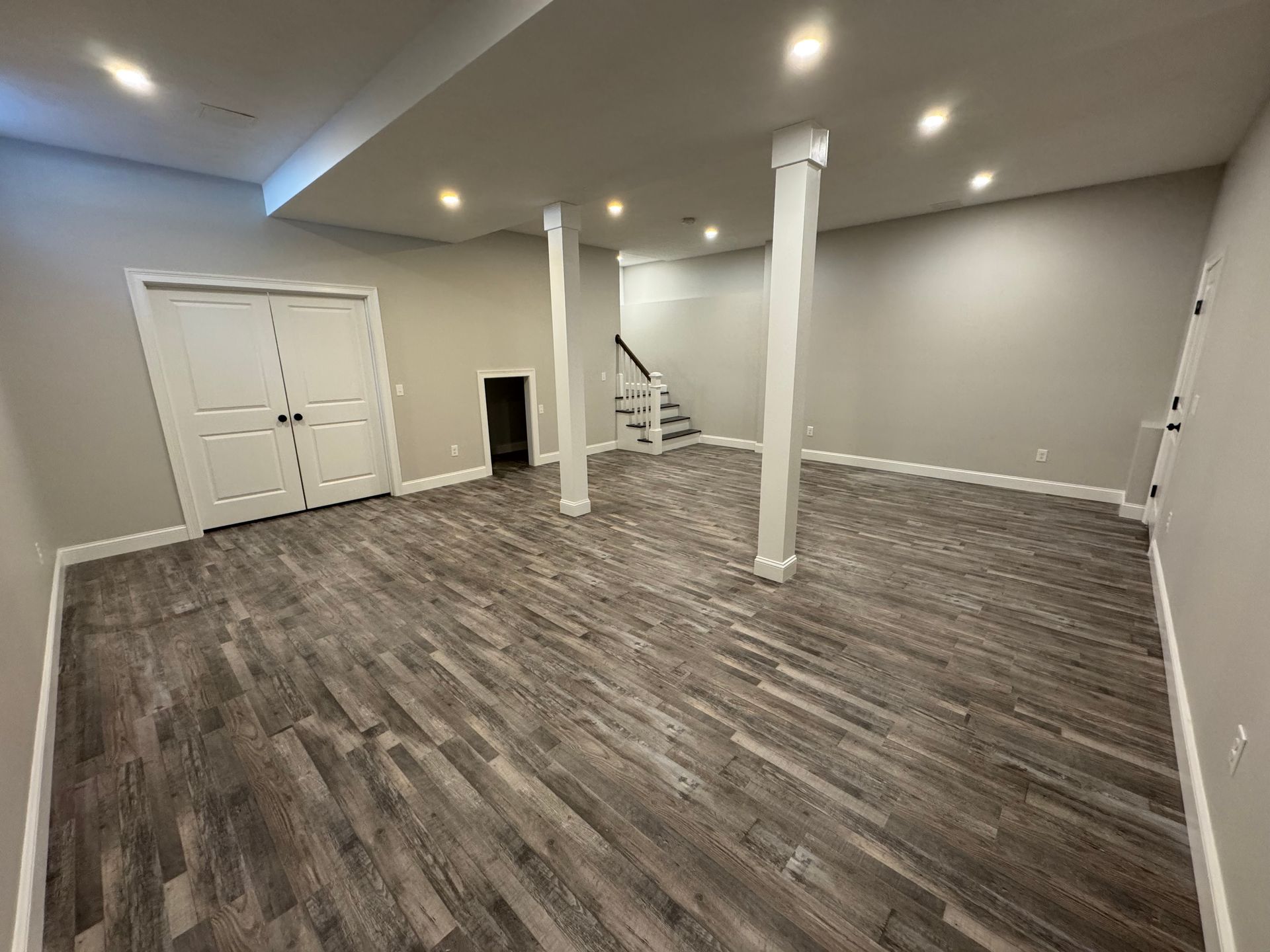 An empty basement with hardwood floors and a staircase.