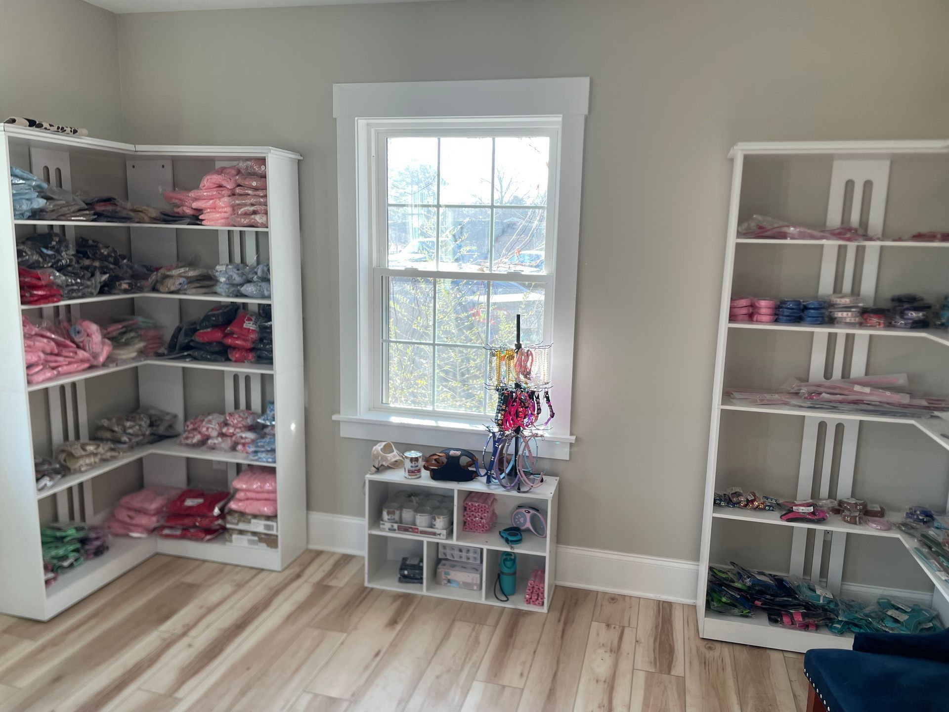 Room with white shelving units displaying clothing, window in center. Wooden floor.