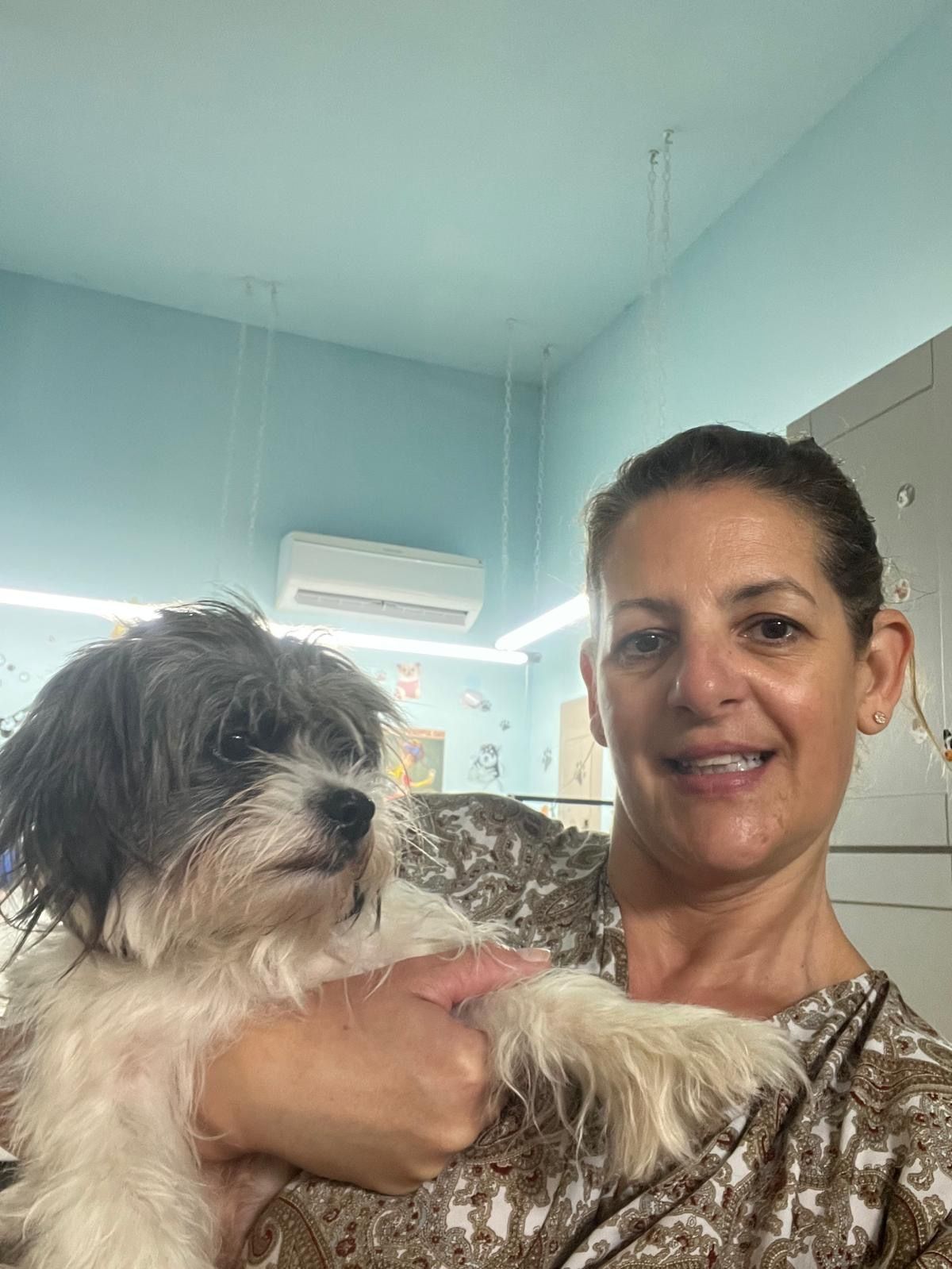 A woman holding a small, fluffy dog indoors. The dog has gray and white fur. Light blue walls.