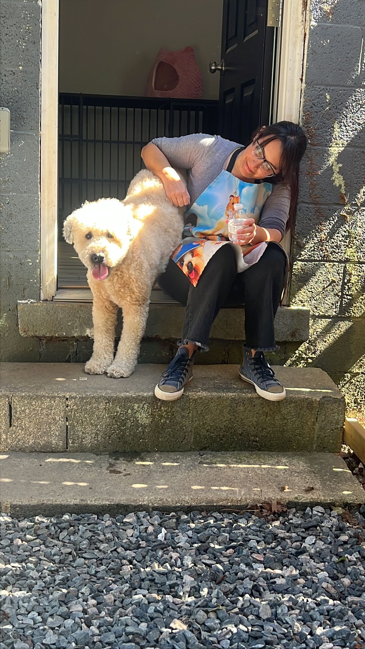 Person sits on stone steps with a fluffy cream dog in front of a house entrance.