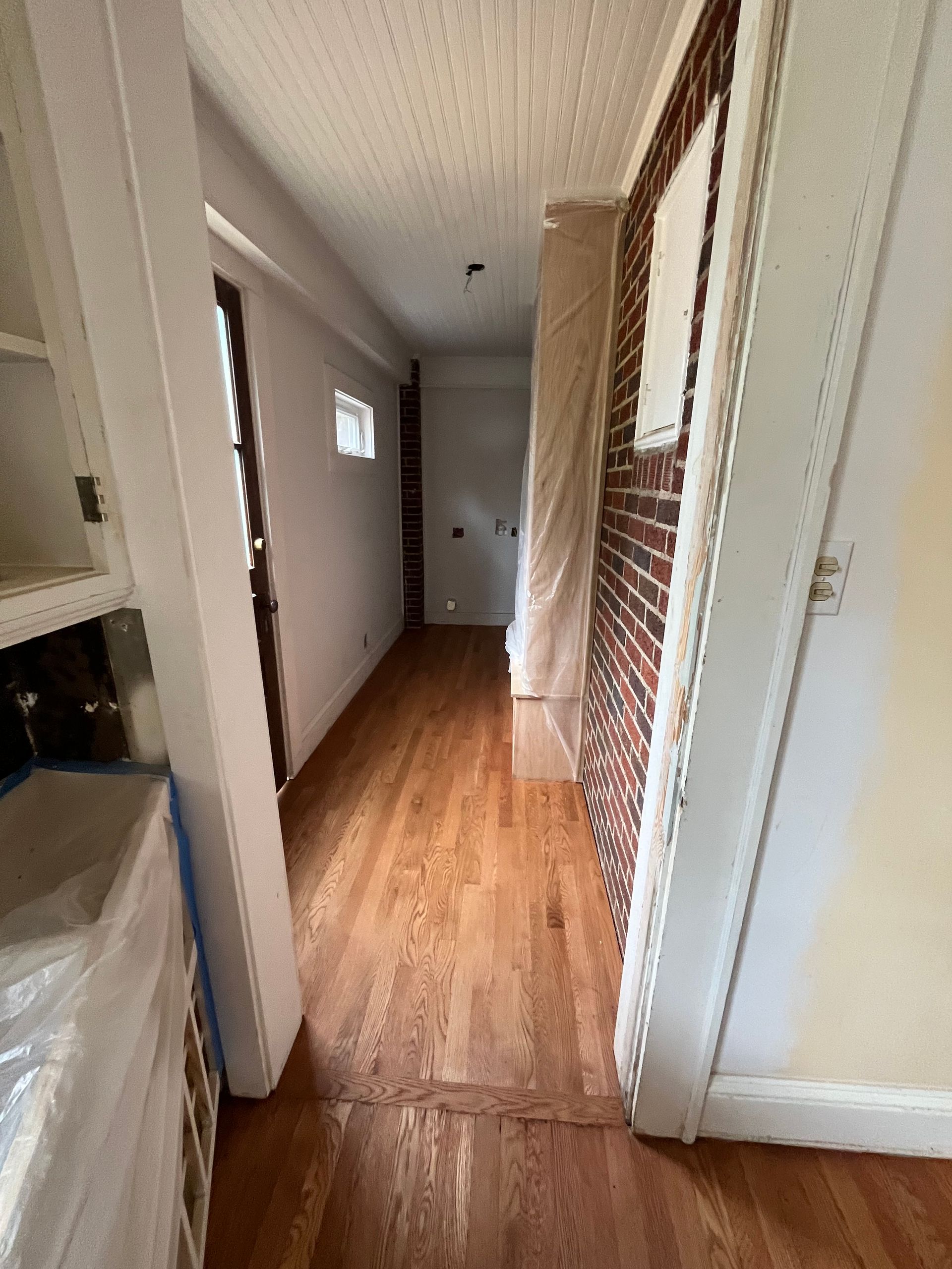 A long hallway with hardwood floors and a brick wall.