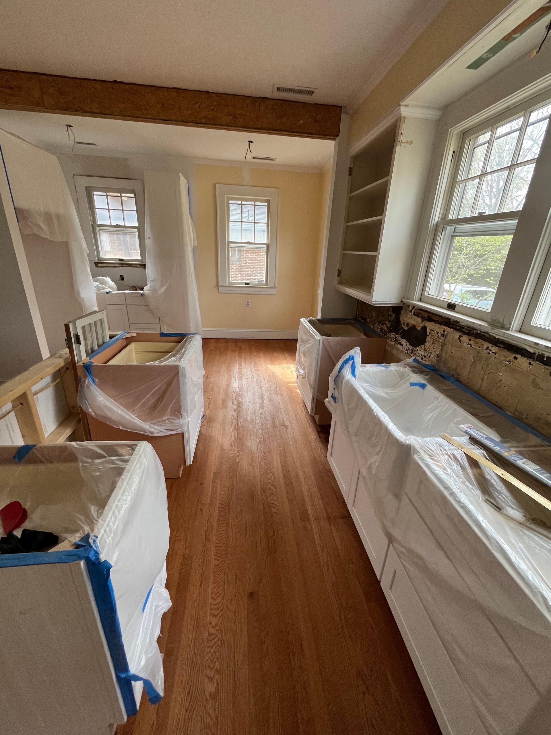 A kitchen under construction with wooden floors and white cabinets.