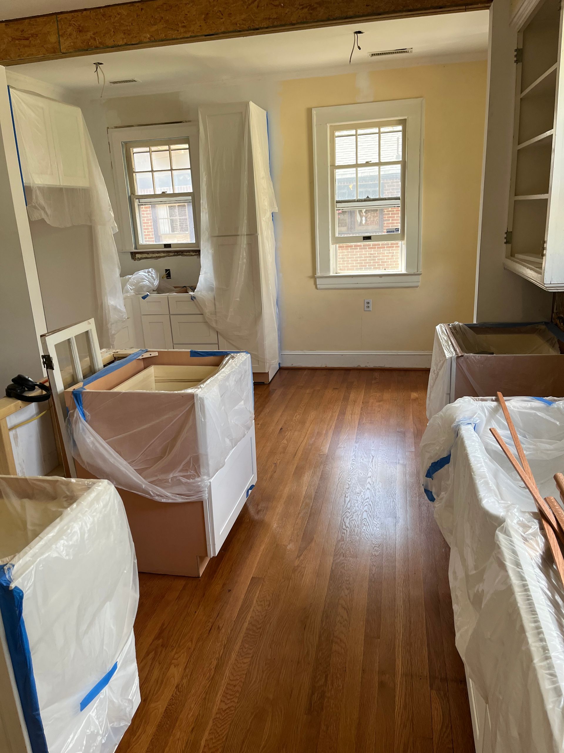 A kitchen is being remodeled and the cabinets are covered in plastic.