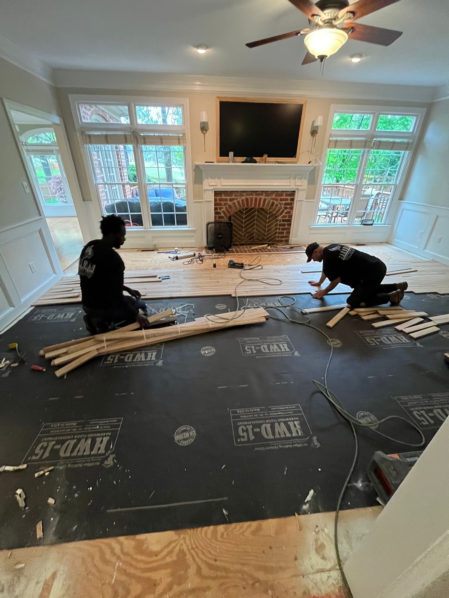 Two men are working on a wooden floor in a living room.