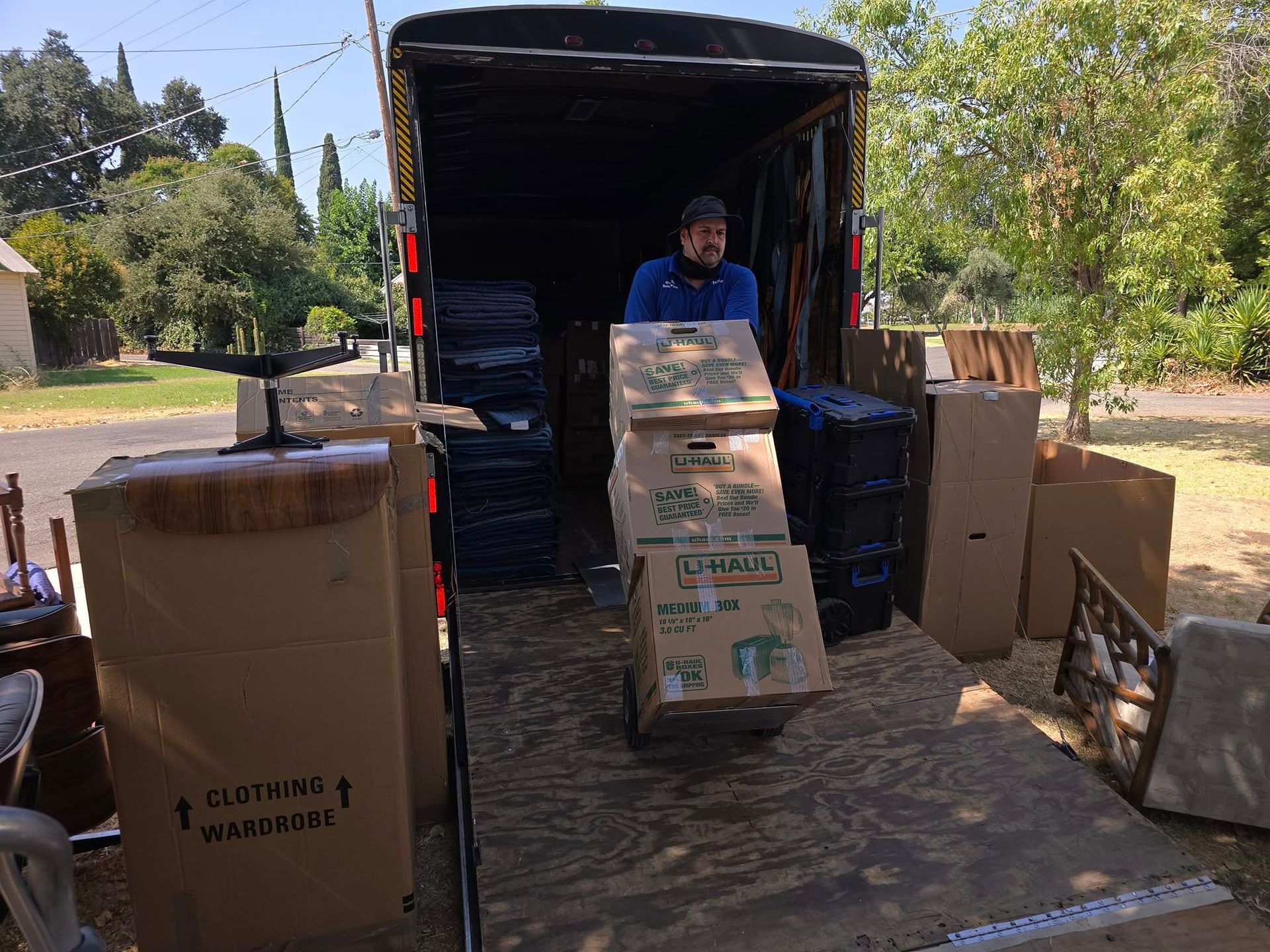 A person loads cardboard boxes into the back of a moving truck parked on a residential street.
