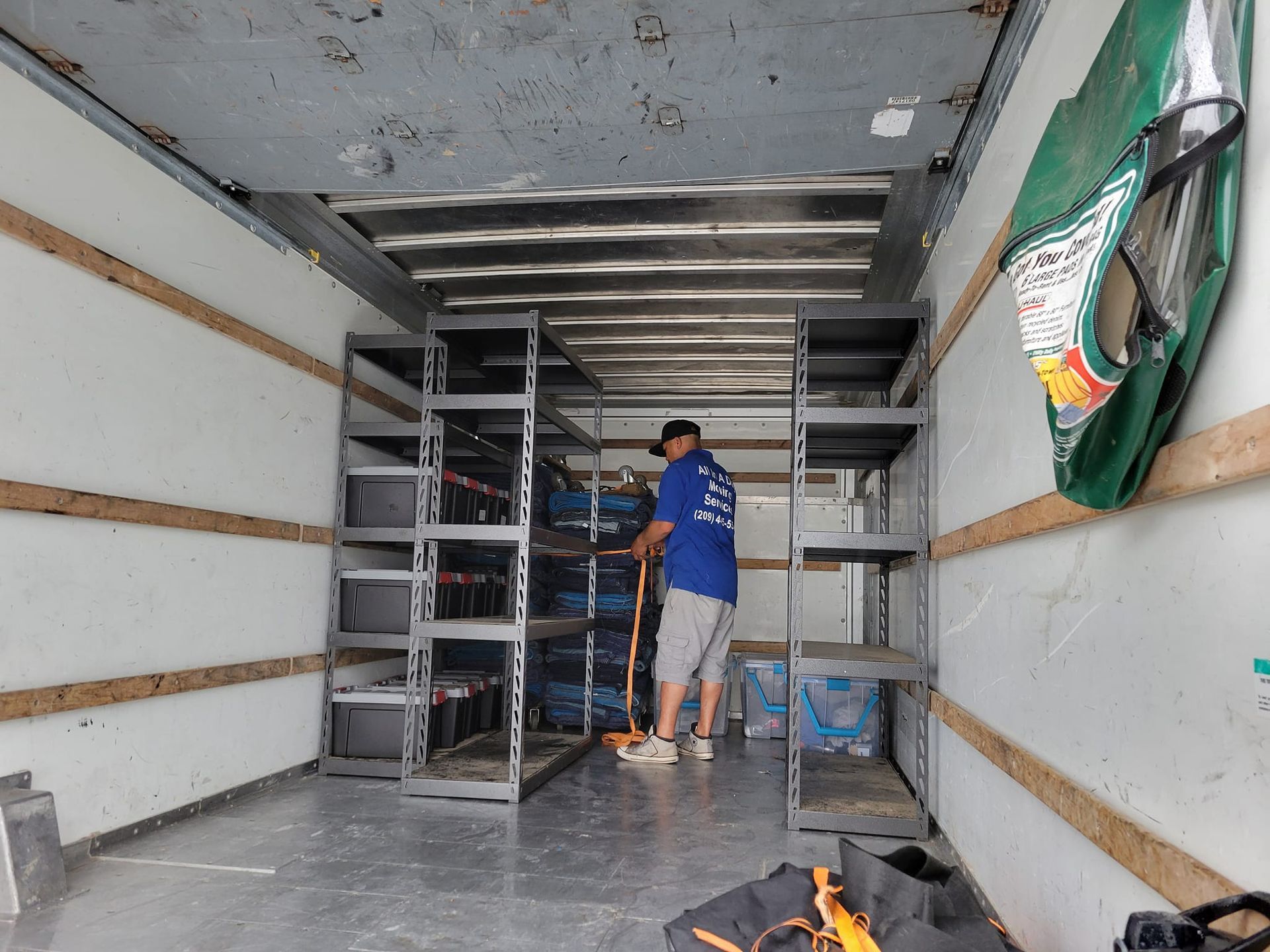 A person in a blue shirt secures cargo inside a truck equipped with metal shelving units.