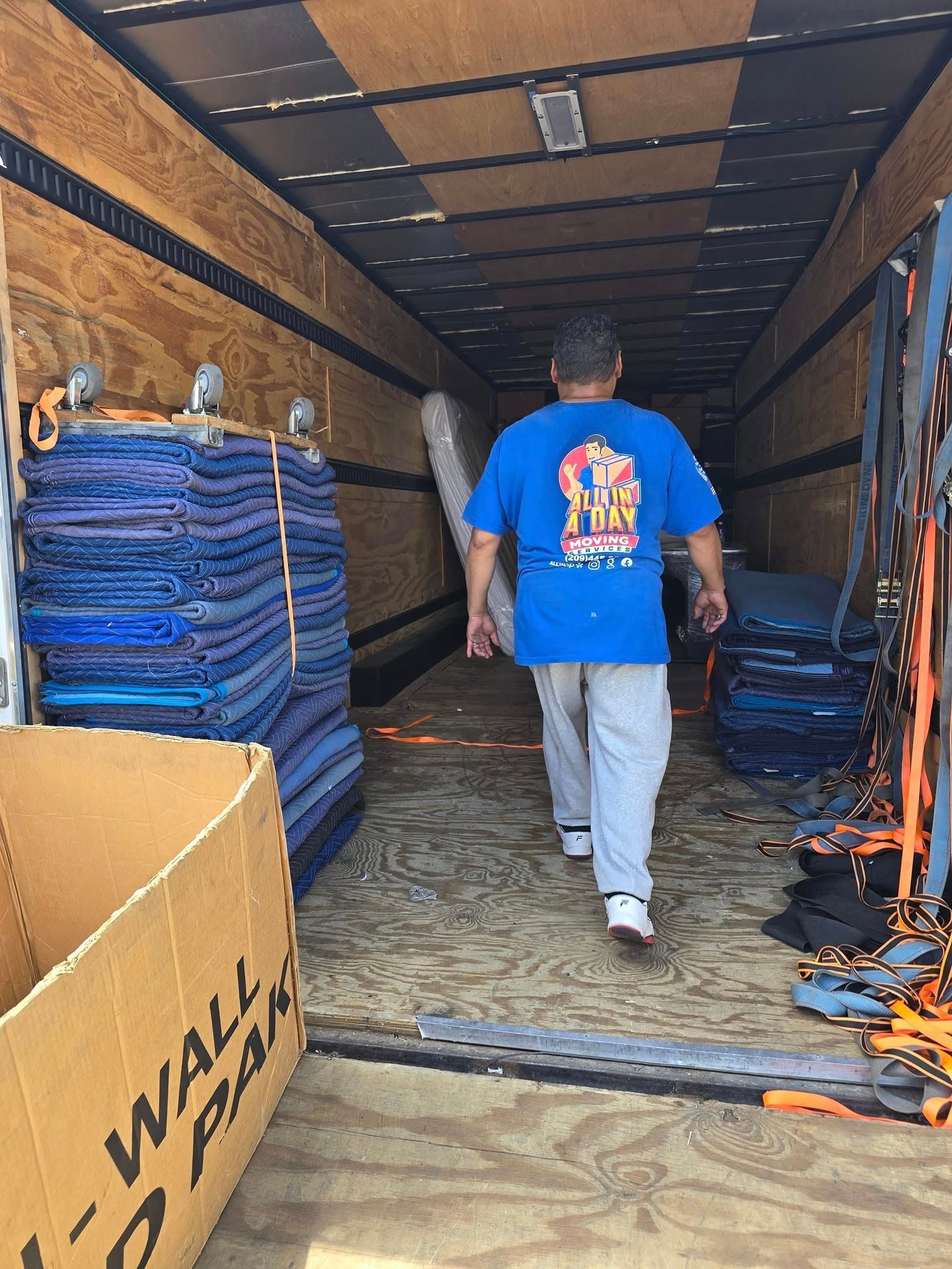 A person in a blue t-shirt walks into a trailer filled with stacked moving blankets and equipment.