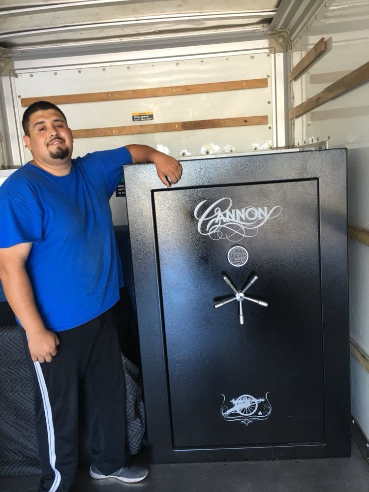 A person in a blue shirt smiling while leaning against a large, black Cannon gun safe inside a truck.