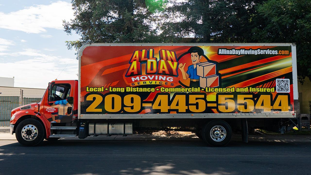 An orange All In A Day Moving truck parked on the street with the company phone number 209-445-5544 displayed on the side.