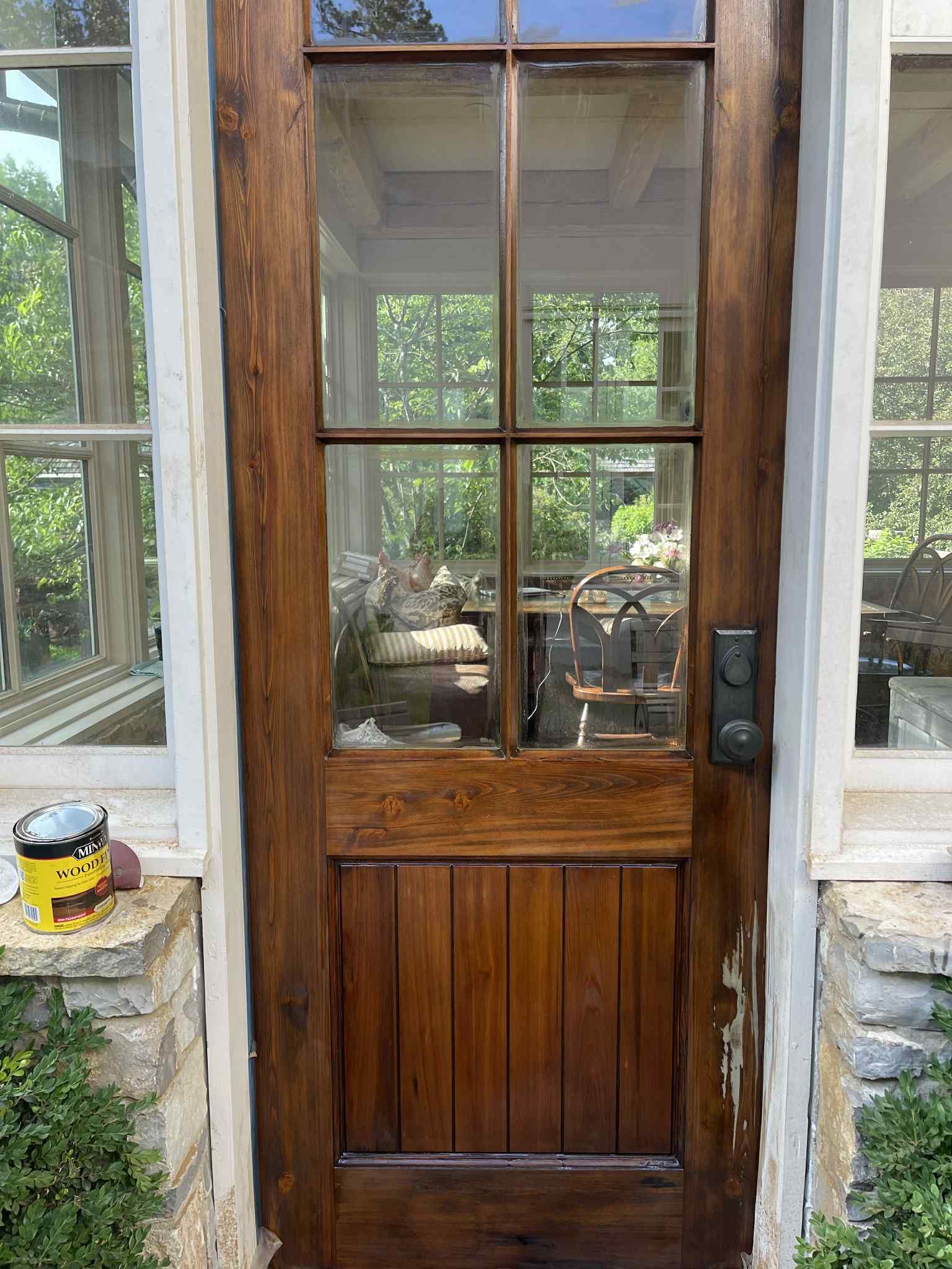 Wooden door with glass panes and wood panel, surrounded by stone and windows.