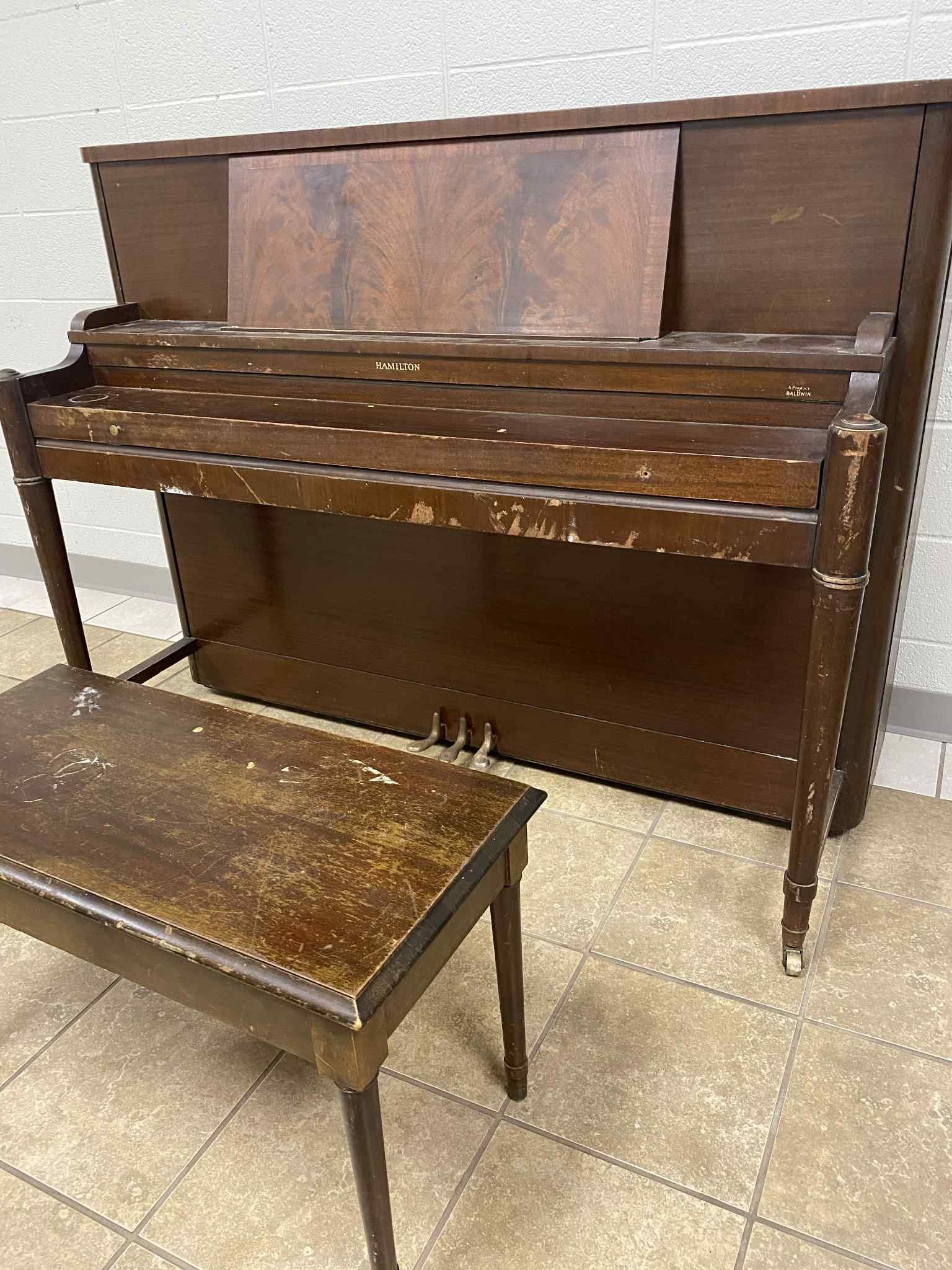 Brown upright piano and bench, both showing significant wear and tear, in a tiled room.