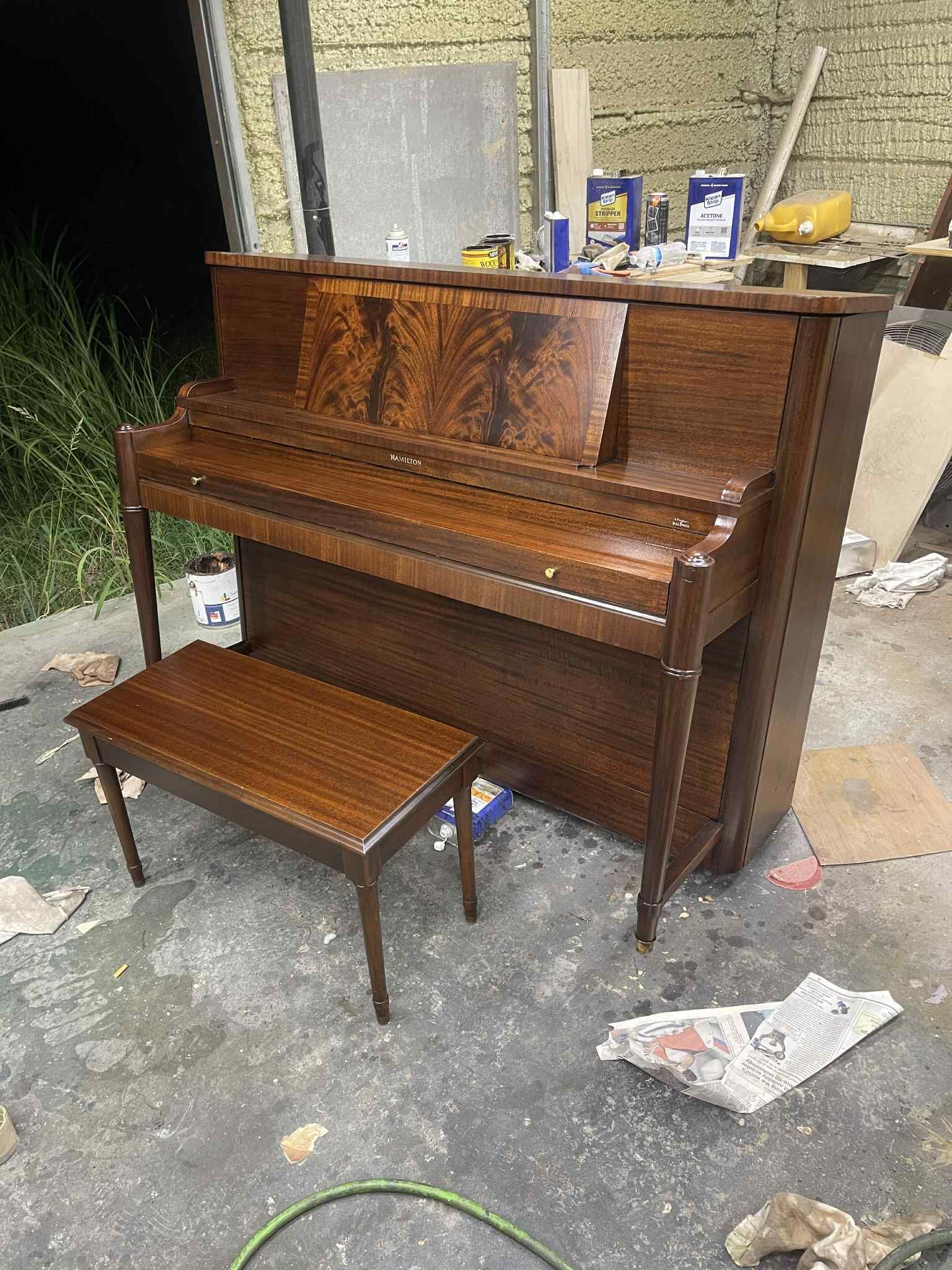 A refinished upright piano with matching bench in a workshop.