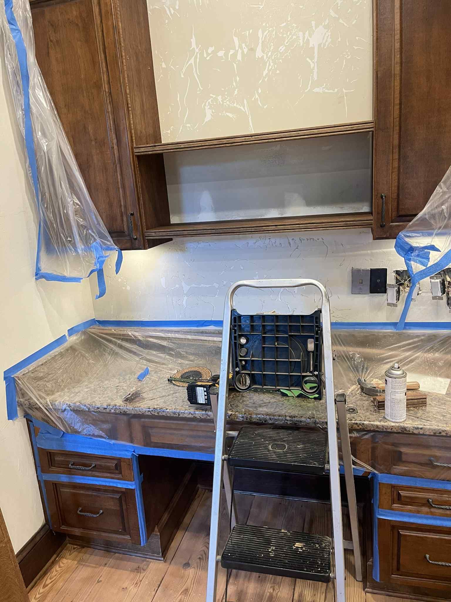 Kitchen cabinets being painted, countertop and bottom cabinets covered.